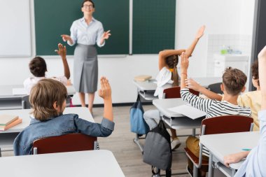 Elleri havada çok kültürlü öğrencilerin arka planı ve sınıftaki tahtaya yakın duran öğretmen.