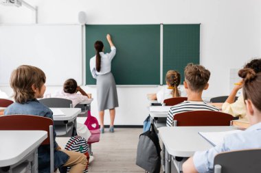 Sınıftaki çok kültürlü öğrencilerin yakınındaki tahtaya yazı yazan öğretmenlerin arka planı