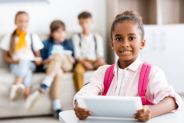 Okulda sınıf arkadaşlarıyla birlikte dijital tablet taşıyan Afrikalı Amerikalı kızın seçici odak noktası. 