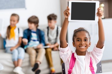 Sınıfta boş ekranlı dijital tablet tutan Afro-Amerikan öğrenci seçici odağı 