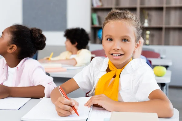 Focus Selettivo Della Studentessa Che Guarda Fotocamera Mentre Scrive Vicino — Foto Stock