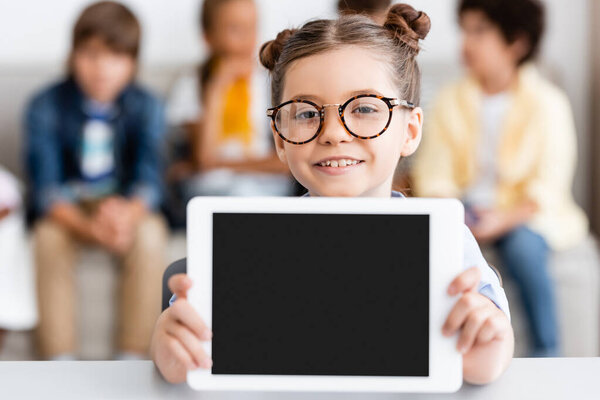 Selective focus of schoolgirl in eyeglasses holding digital tablet at desk 