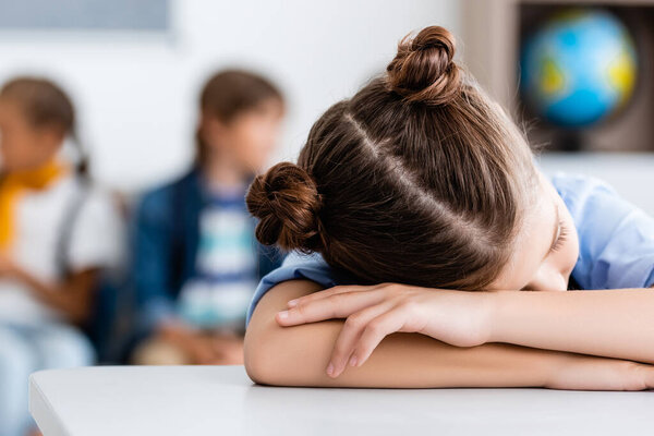 Selective focus of schoolgirl sleeping at desk in classroom 