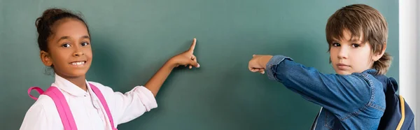 Panoramic Shot Multiethnic Schoolchildren Backpacks Pointing Chalkboard — Stock Photo, Image