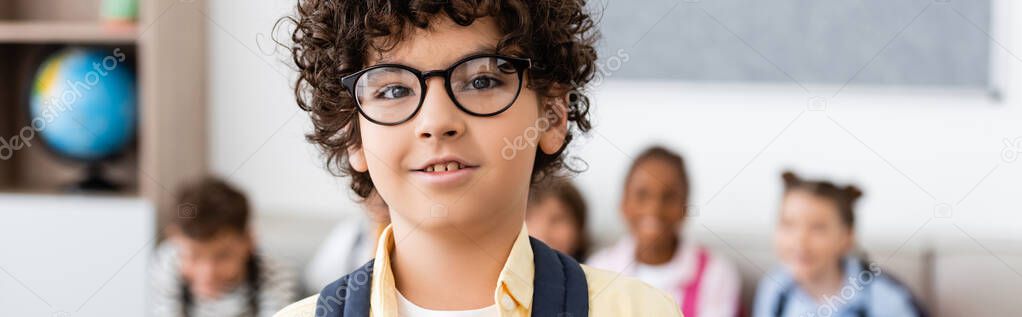 Panoramic shot of muslim schoolboy looking at camera in classroom 