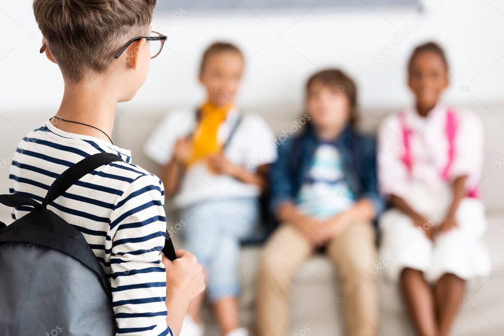 Selective focus of schoolboy with backpack standing near multiethnic friends in classroom 