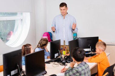 Sınıftaki bilgisayarların yakınındaki öğretmenlere bakan öğrencilerin seçici odak noktası 