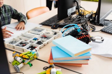 Selective focus of schoolboy sitting near parts of robots and computers in school  clipart