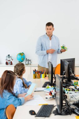 Sınıftaki kız öğrencilerin ve bilgisayarların yanındaki robotu işaret eden seçmeli bir öğretmen. 