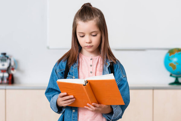 Schoolgirl with backpack reading book in stem school  