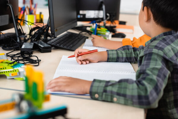 Selective focus of asian schoolboy with pen sitting near computers in stem school 