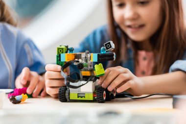 Selective focus of schoolgirl programing robot near friend in stem school  clipart