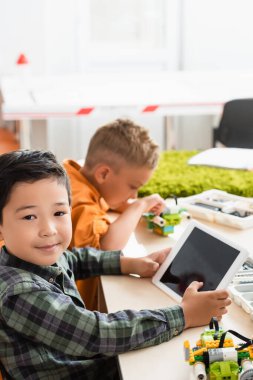Asyalı bir çocuğun dijital tablet taşıdığı seçici odak noktası kök okulunda arkadaş modellik yapan robot. 
