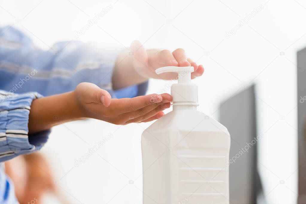 Cropped view of schoolgirl using hand sanitizer in classroom 