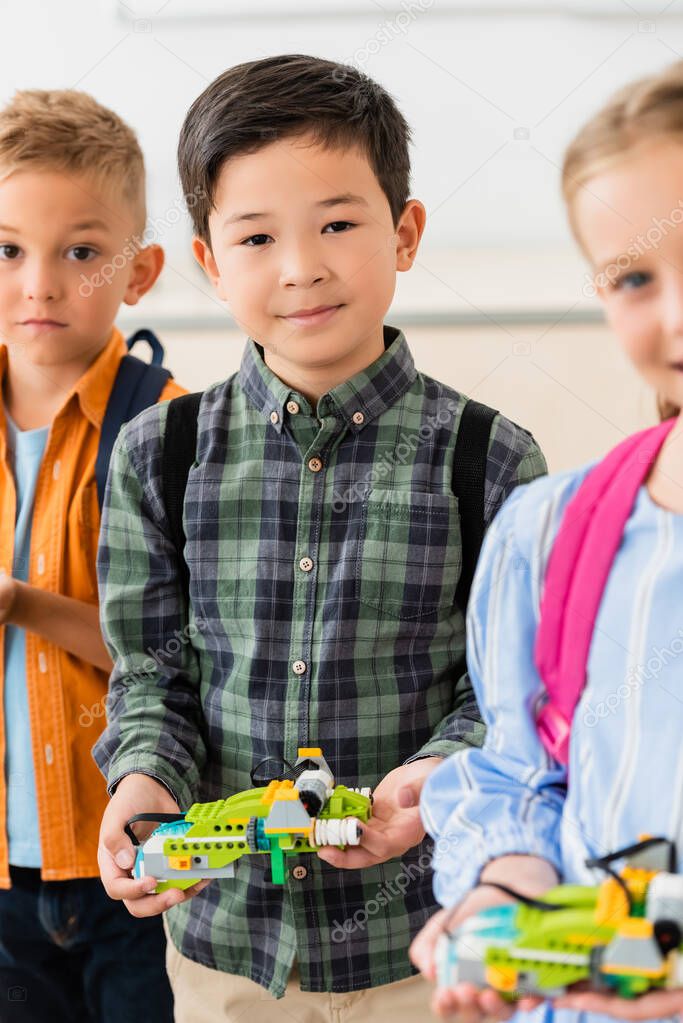 Selective focus of asian schoolboy holding robot near friends in school 
