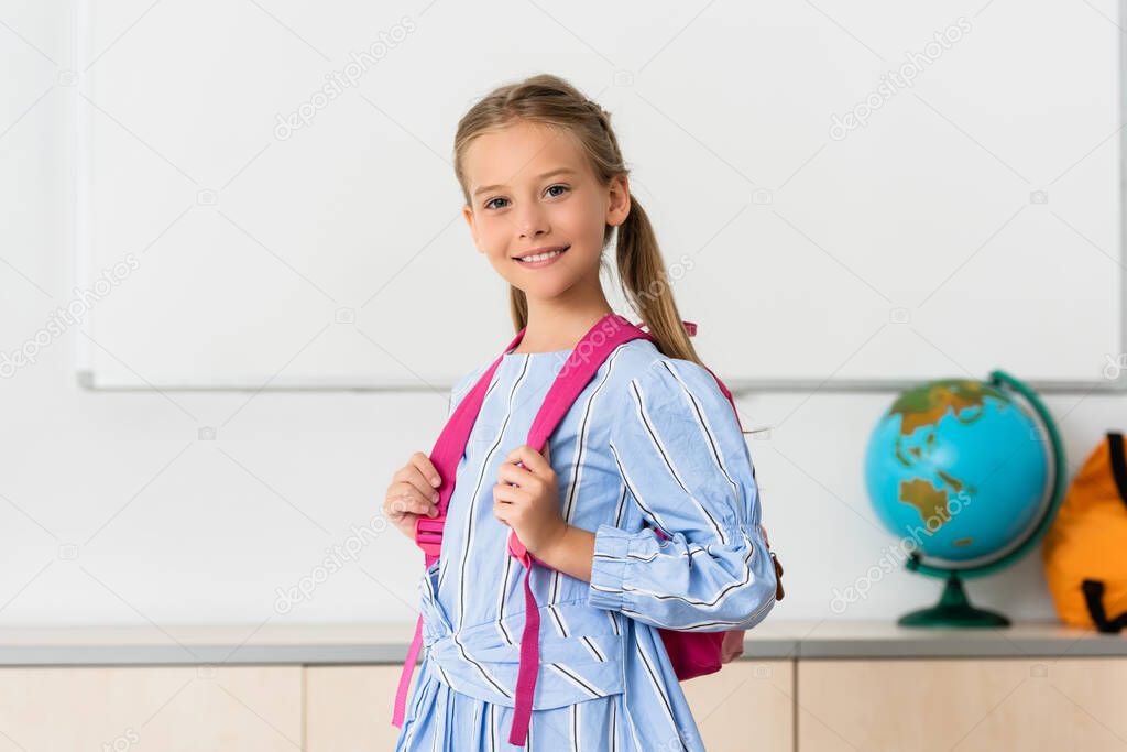 Schoolgirl with backpack looking at camera in classroom 