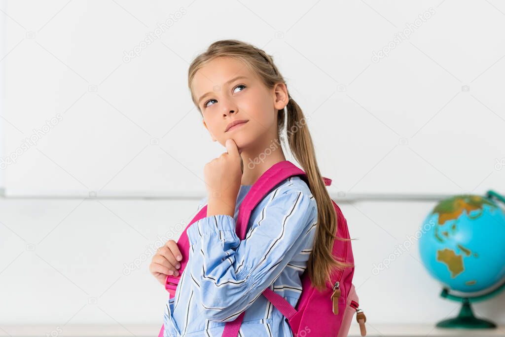 Pensive schoolgirl with backpack looking away in classroom 