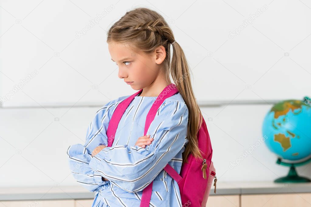 Serious schoolgirl with backpack looking away in classroom 