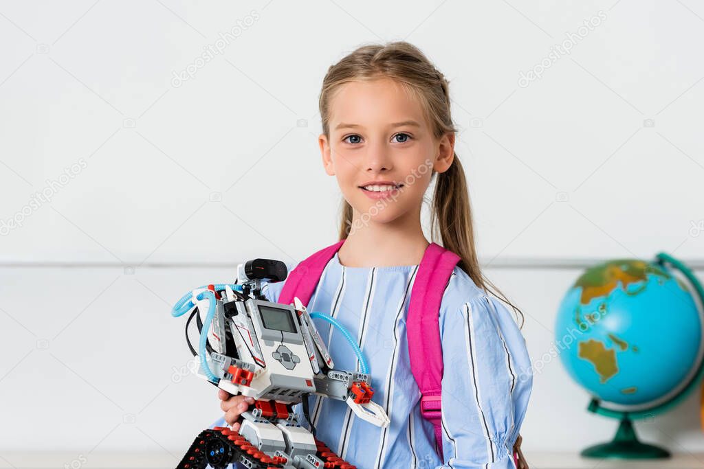 Schoolgirl holding robot and looking at camera in classroom 