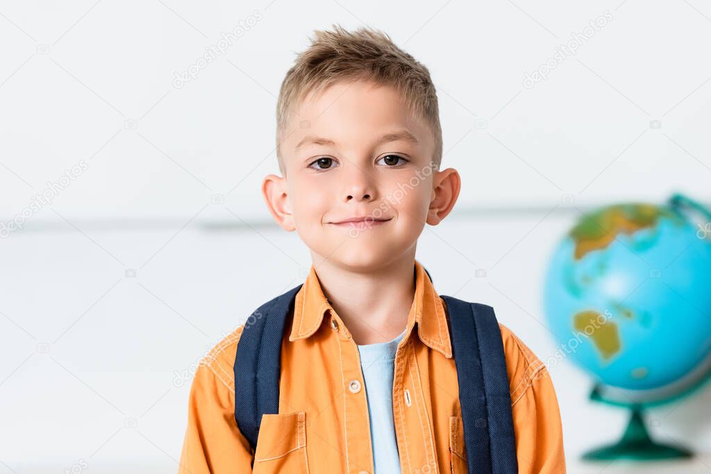 Schoolkid with backpack looking at camera in classroom 