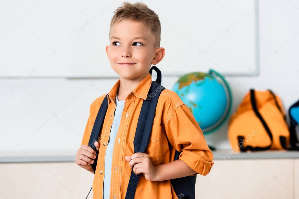 Schoolboy holding backpack while looking away in classroom 