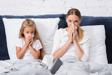 Selective focus of sick mother and daughter holding napkins while having snuffle on bed  clipart