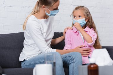 Evde tıbbi maskeli çocuğu kucaklayan annenin seçici odağı 