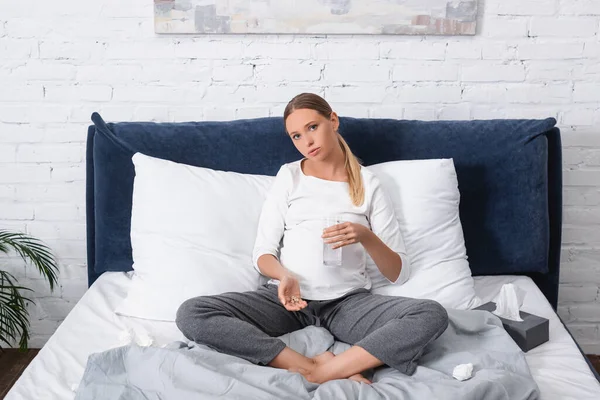 孕妇在床上餐巾纸附近拿着一杯水和药丸 — 图库照片