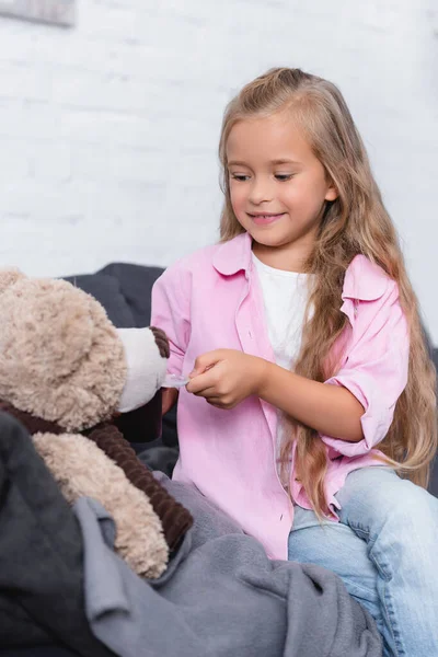 ソファの上に柔らかいおもちゃの近くにシロップの子供の保持スプーンの選択的な焦点 — ストック写真