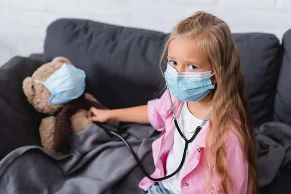 Enfoque Selectivo Niña Máscara Médica Celebración Estetoscopio Cerca Oso Peluche —  Fotos de Stock