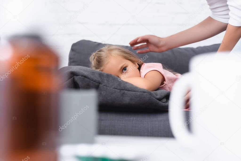 Selective focus of sick child looking at camera near mother on couch 