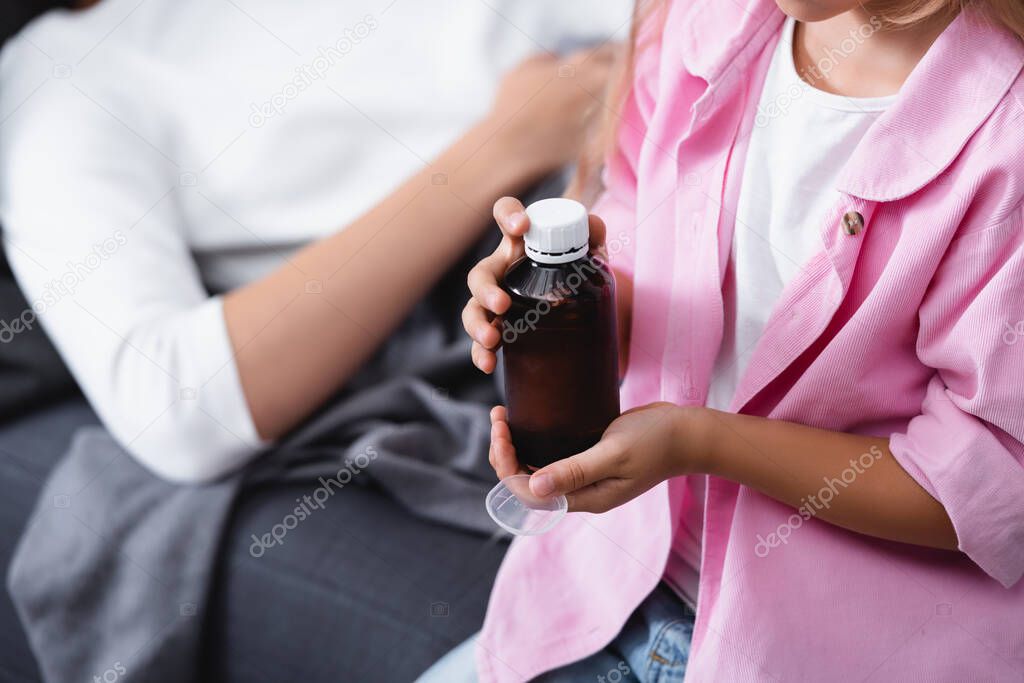 Cropped view of child holding bottle of syrup and spoon near ill mother 