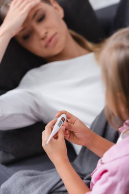 Termometreyi tutan çocuğun seçici odak noktası annesinin alnına dokunması. 