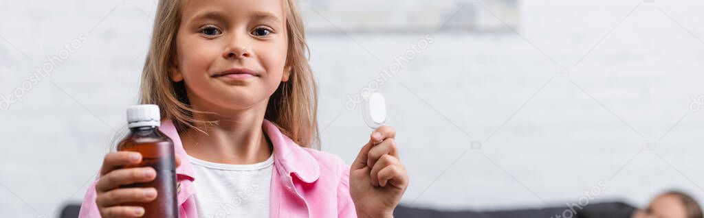 Panoramic shot of child holding bottle of syrup and spoon at home 