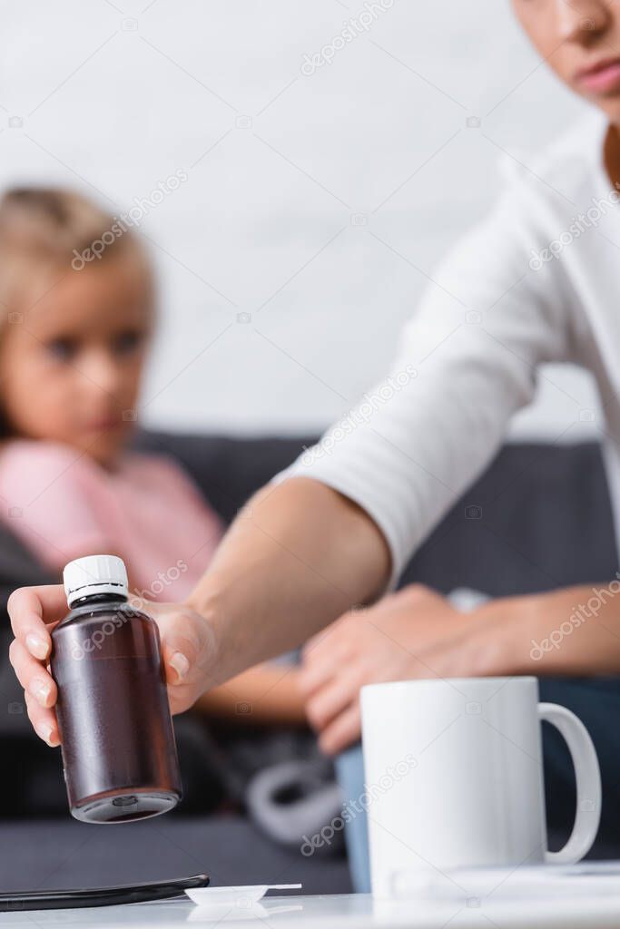 Selective focus of woman taking bottle of syrup near sick child at home 