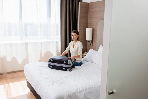 Młoda Kobieta Siedząca Łóżku Oglądająca Bagaż Pokoju Hotelowym — Zdjęcie stockowe