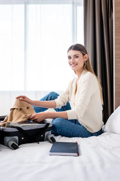 Young Woman Sitting Bed Holding Clothing Luggage Hotel Room — Stock Photo, Image