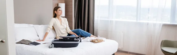 一个全景的概念 就是年轻女人在酒店里看着身边的笔记本和行李 — 图库照片