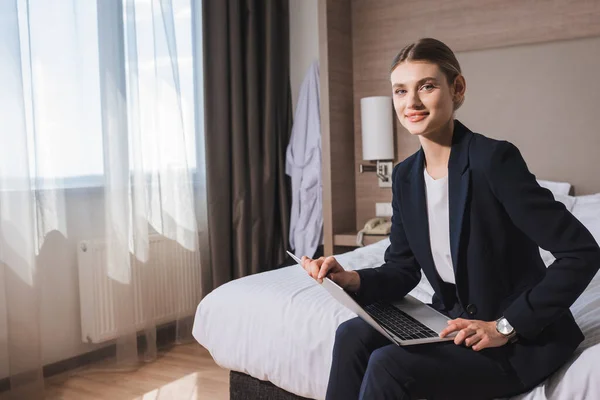 Nöjd Ung Kvinna Kostym Sitter Sängen Med Laptop Hotellrummet — Stockfoto