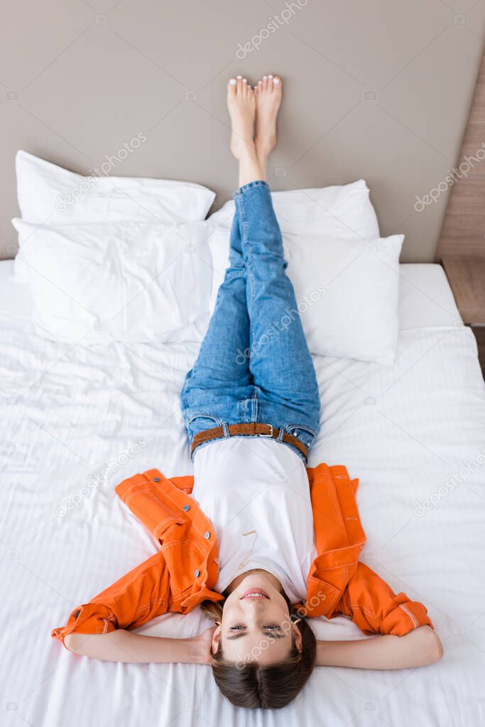 high angle view of barefoot young woman in jeans resting on bed in hotel room