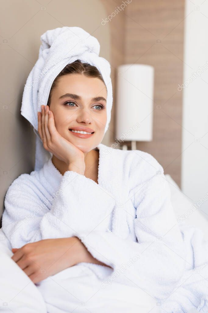 dreamy woman in towel and white bathrobe looking away in hotel room
