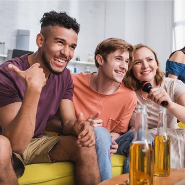 Heyecanlı Afrikalı Amerikalı adamın seçici odak noktası. Çok kültürlü arkadaşlarının yanında baş parmağı beliriyor ve karaoke söylüyor.