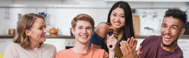 Afrikalı Amerikalı bir adamın panoramik mahsulü çok ırklı arkadaşları karaoke yaparken alkışlıyor.
