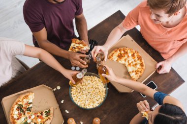 Parti sırasında pizzanın yanında bira şişelerini tokuşturan çok kültürlü arkadaşların üst görüntüsü.