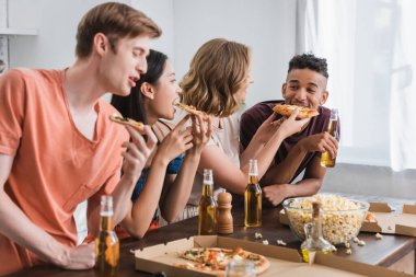 Parti sırasında pizza yiyen neşeli çoklu etnik arkadaşların seçici odağı