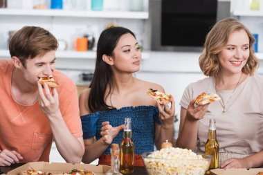 Neşeli çok kültürlü arkadaşlar patlamış mısır kasesinin yanında pizza yiyorlar. 