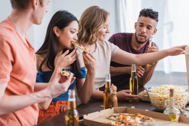 Parti sırasında pizza yiyen heyecanlı çok kültürlü arkadaşların seçici odağı.