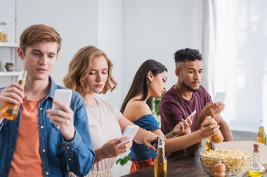 Parti sırasında bira ve patlamış mısırın yanında akıllı telefonlarda sohbet eden çok kültürlü genç arkadaşların seçici odağı.