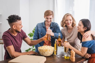 Afrikalı Amerikalı bir adam, çok kültürlü kadınlarla parti sırasında arkadaşına bir şişe bira veriyor.