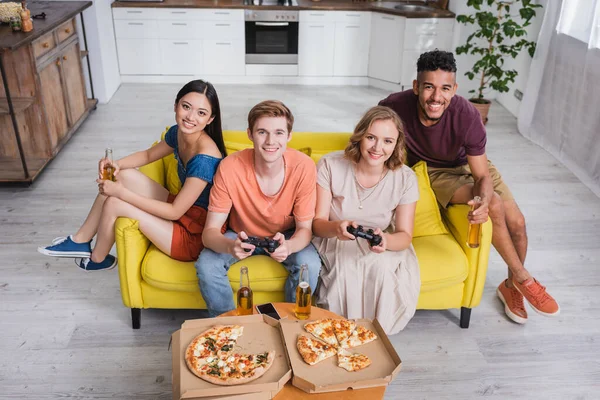 KYIV, UKRAINE - 28 Temmuz 2020: Bira tutan ve pizza yanında oyun oynayan çok kültürlü arkadaşların yüksek açılı görüntüsü